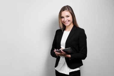 Bir takım elbise ve ceket beyaz bir arka plan üzerinde elinde bir tablet ile güzel bir gülümseyen kadın sarışın portresi. Bir öğrenci ya da bir iş kadını çalışıyor.