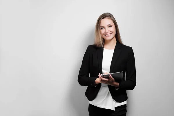 Portret van een mooie lachende vrouw blonde met een tablet in haar handen in een pak en de jas op een witte achtergrond. Een student of een zakenvrouw werkt. — Stockfoto