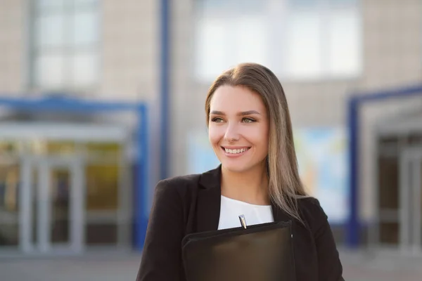 Joven chica hermosa en la calle junto al edificio en una chaqueta y con un cuaderno . — Foto de Stock