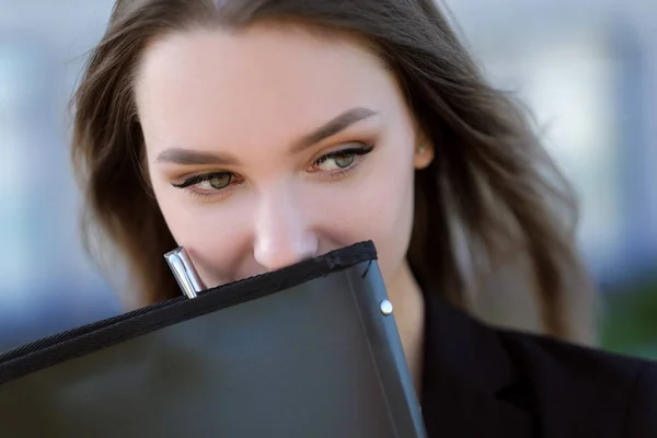 Joven chica hermosa en la calle junto al edificio en una chaqueta y con un cuaderno . — Foto de Stock