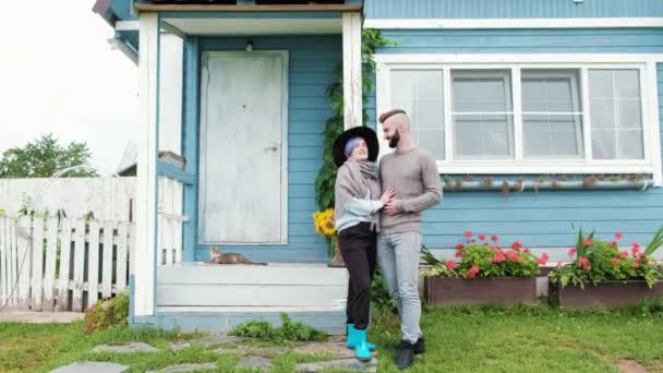 Jeune famille, homme et femme sur fond de maison de village en bois bleu . — Video