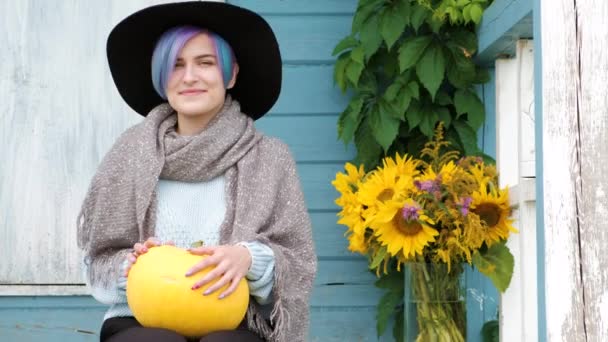 A young beautiful woman is sitting on porch of country house with pumpkins. — Stock Video