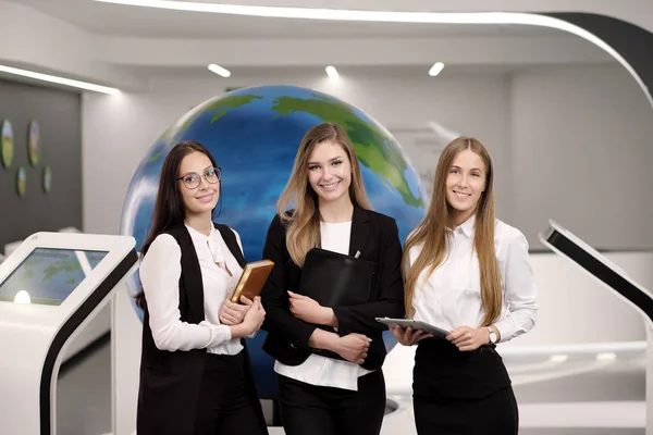 Drie mooie jonge meisjes in het kantoor met een tablet op de achtergrond van de hele wereld. Bedrijfsleven en wetenschap. — Stockfoto