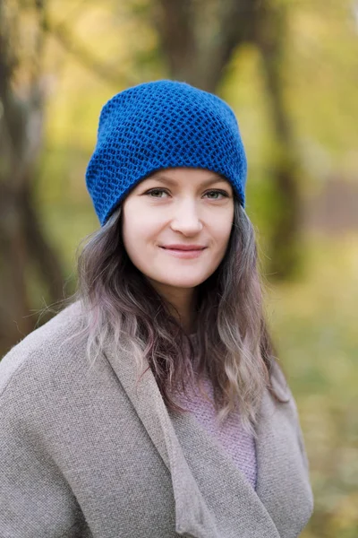 The girl in a coat and blue hat on a background of autumn trees and maple leaves. — Stock Photo, Image