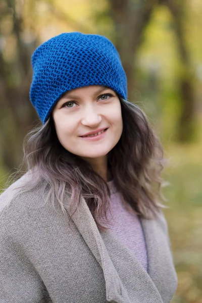 The girl in a coat and blue hat on a background of autumn trees and maple leaves. — Stock Photo, Image