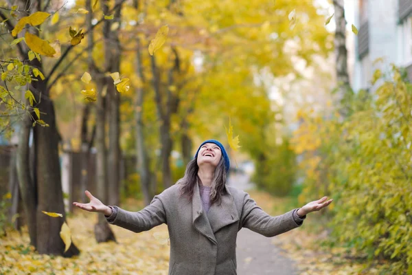 Sonbahar ağaçlar ve akçaağaç arka plan üzerinde kat ve mavi şapkalı kız bırakır.