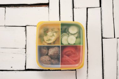 Ayrı bir kapta pişmiş yemek. Haşlanmış patates, salatalık, domates ve biftek köftesi.