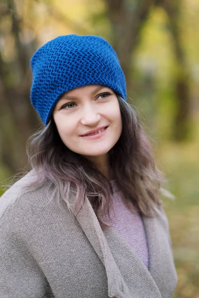 The girl in a coat and blue hat on a background of autumn trees and maple leaves. — Stock Photo, Image