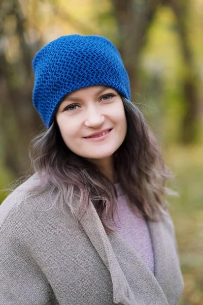 The girl in a coat and blue hat on a background of autumn trees and maple leaves. — Stock Photo, Image