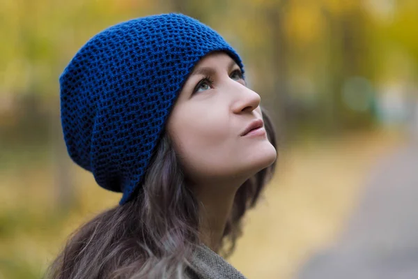 Das Mädchen in Mantel und blauem Hut auf einem Hintergrund aus Herbstbäumen und Ahornblättern. — Stockfoto