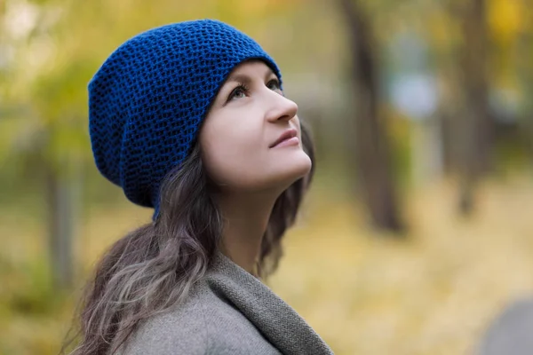 Das Mädchen in Mantel und blauem Hut auf einem Hintergrund aus Herbstbäumen und Ahornblättern. — Stockfoto