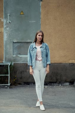 Beton duvar arka plan üzerinde bir T-shirt ve kot ceketli uzun saçlı Genç güzel kız.