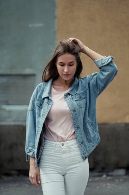Beton duvar arka plan üzerinde bir T-shirt ve kot ceketli uzun saçlı Genç güzel kız.