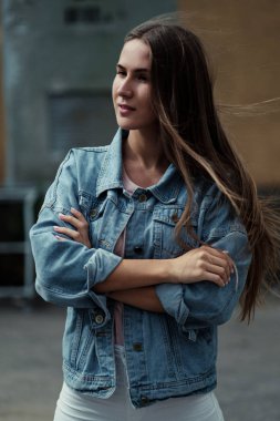 Beton duvar arka plan üzerinde bir T-shirt ve kot ceketli uzun saçlı Genç güzel kız.