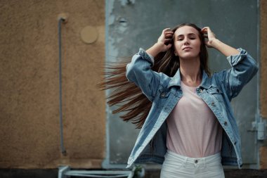 Beton duvar arka plan üzerinde bir T-shirt ve kot ceketli uzun saçlı Genç güzel kız.