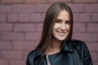 Genç güzel beyaz kız bir tuğla duvar arka plan üzerinde siyah deri ceketli poz.