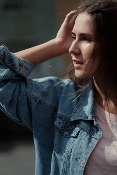 Junge schöne Mädchen mit langen Haaren in einem T-Shirt und Jeansjacke auf dem Hintergrund der Vintage-Betonwand. — Stockfoto