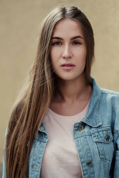 Giovane bella ragazza con i capelli lunghi in una t-shirt e giacca di jeans sullo sfondo di muro di cemento vintage . — Foto Stock