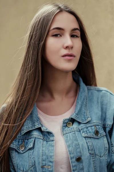 Giovane bella ragazza con i capelli lunghi in una t-shirt e giacca di jeans sullo sfondo di muro di cemento vintage . — Foto Stock