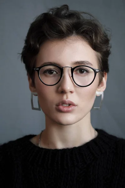 年轻美丽的女孩与短卷发在眼镜和黑色休闲服, 工作室肖像. — 图库照片