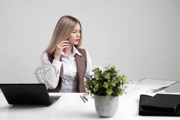 Chica rubia en un traje de negocios trabaja en una computadora en una oficina blanca brillante . — Foto de Stock