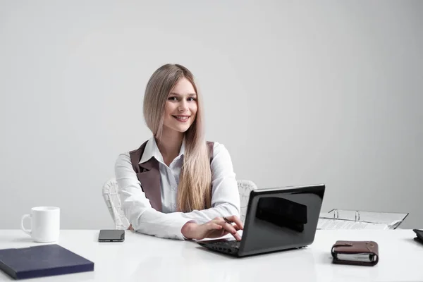 Ξανθιά κοπέλα σε ένα επαγγελματικό κοστούμι λειτουργεί σε έναν υπολογιστή σε ένα λευκό φωτεινό γραφείο. — Φωτογραφία Αρχείου