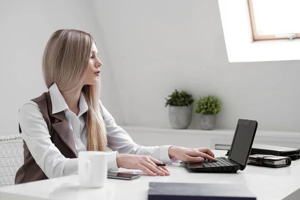İş takım elbiseli sarışın kız beyaz parlak bürosunda bir bilgisayarda çalışır. — Stok fotoğraf