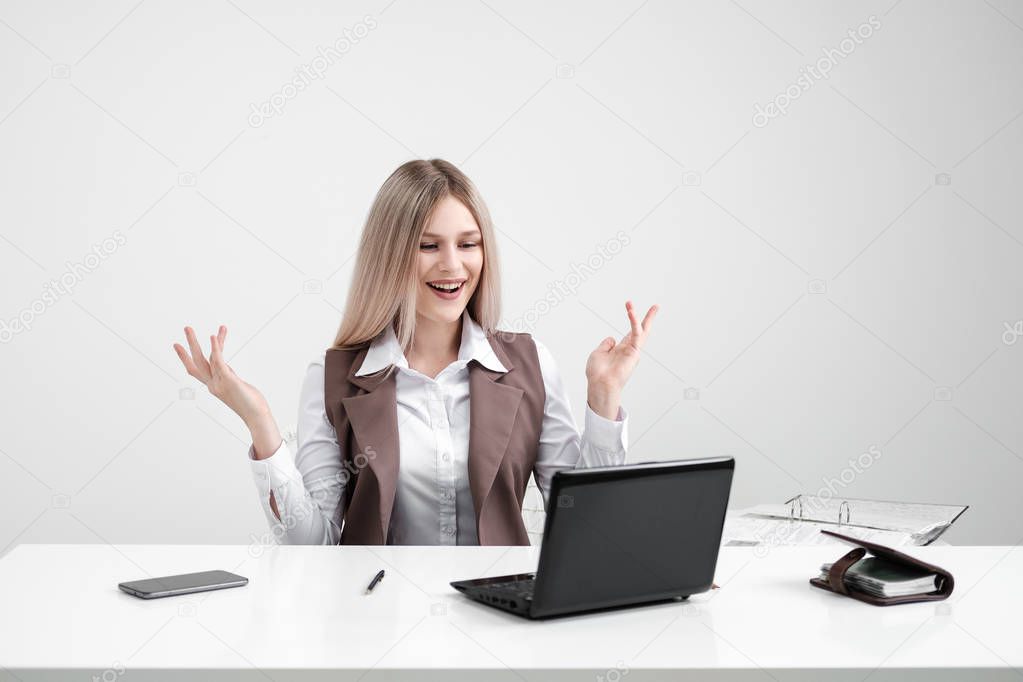 Caucasian girl sitting at the table at the computer in the office. Rejoices and smiles.