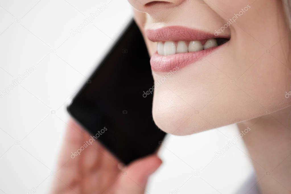 Close-up of the mouth and lips of a woman talking on a smartphone on a white background.