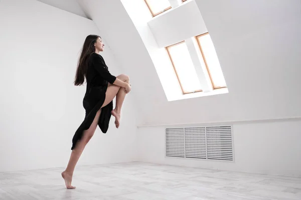 Una giovane ballerina vestita di nero si allunga vicino alla finestra. Sala bianca, la classe operaia, asana yoga . — Foto Stock