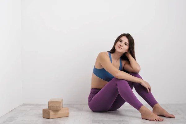 Junge brünette Frau in lila Leggings und Sport-T-Shirt macht Übungen auf dem Boden. balanciert auf den Blöcken und in der Nähe der Mauer. Weißes Zimmer. — Stockfoto