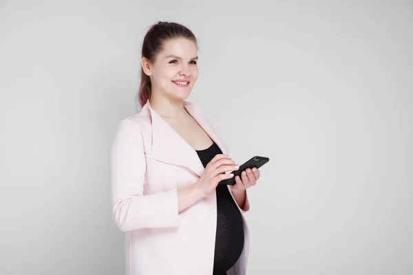 Молодая беременная женщина печатает на смартфоне. На белом фоне . — стоковое фото