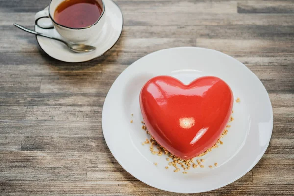 Красный торт со льдом в форме сердца. Бурый деревянный стол и чашка чая на заднем плане . — стоковое фото