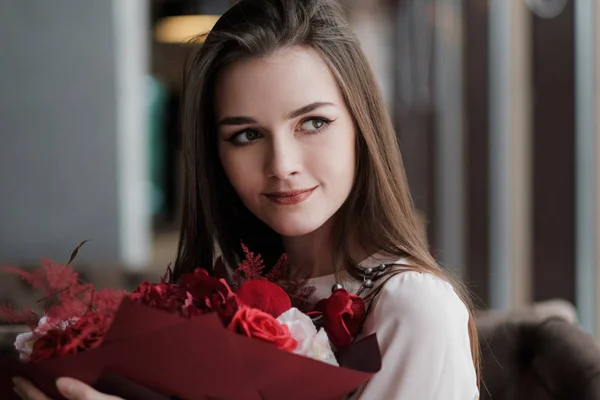 La ragazza è seduta in un caffè con un mazzo di fiori rossi, peonie, rose e crisantemi . — Foto Stock