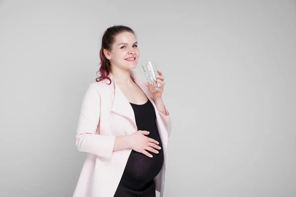 Una chica embarazada sostiene un vaso de agua y bebe . —  Fotos de Stock