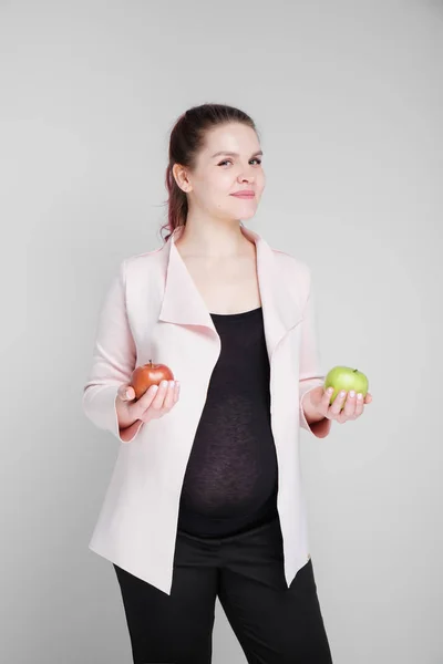 Uma mulher grávida está segurando maçãs verdes e vermelhas . — Fotografia de Stock