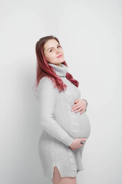 Une femme enceinte avec des cheveux cramoisis colorés dans un pull gris tricoté . — Photo