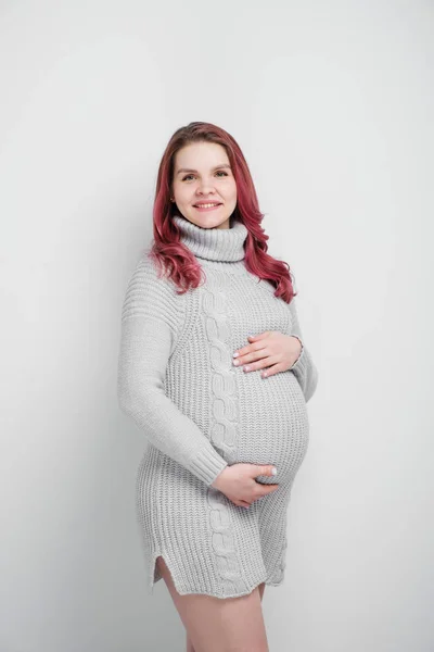 Uma mulher grávida com cabelos carmesim coloridos em um pulôver cinza de malha . — Fotografia de Stock