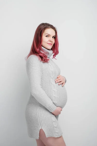 A pregnant woman with colored crimson hair in a knitted gray pullover. — Stock Photo, Image