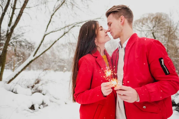 Молодой человек и женщина целуются зимой в парке. Красная одежда. В руках горящих фейерверков. Романтическое веселье . — стоковое фото