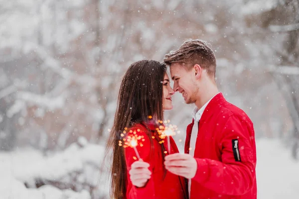 Молодой человек и женщина целуются зимой в парке. Красная одежда. В руках горящих фейерверков. Романтическое веселье . — стоковое фото