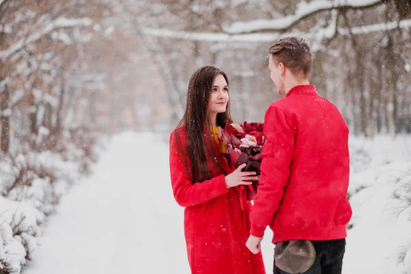 Data kochanków z moim park w zimie. Bukiet czerwonych kwiatów, chodzić, przytulić, pocałować, śmiech w romantycznej atmosferze. Portret para, mąż i żona. Czerwone Kurtki i Płaszcze. — Zdjęcie stockowe