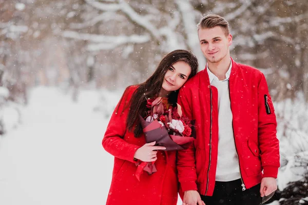 Sebuah tanggal pecinta dengan taman saya di musim dingin. Sebuah karangan bunga merah, berjalan, memeluk, mencium, tertawa dalam pengaturan romantis. Potret pasangan, suami dan istri. Jaket merah dan mantel . — Stok Foto