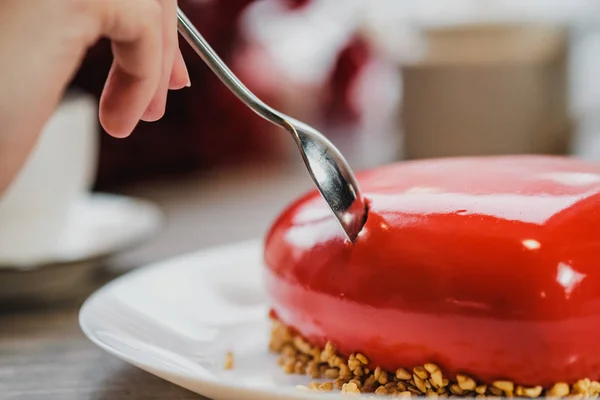 Torta rossa a forma di cuore è sul tavolo. Due mani con cucchiai, maschio e femmina, si allungano in una torta . — Foto Stock