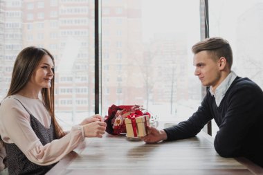 Genç bir adam bir kıza, eşi, pencere kenarındaki bir kafede bir hediye bir kırmızı kurdele ile verir.