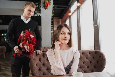 Genç bir adam arkadaşına, karısı, pencere kenarındaki bir kafede bir buket kırmızı çiçek verir.