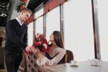 Genç bir adam arkadaşına, karısı, pencere kenarındaki bir kafede bir buket kırmızı çiçek verir.