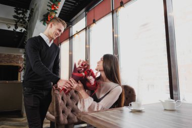 Genç bir adam arkadaşına, karısı, pencere kenarındaki bir kafede bir buket kırmızı çiçek verir.