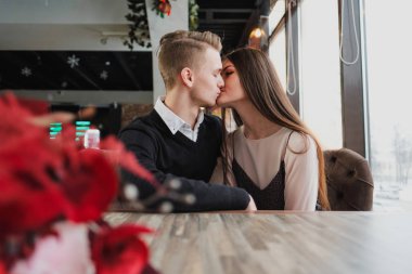 Genç çift sevgi, erkek ve kadın bir kafede romantik bir tarih. Pencerenin yanındaki bir masada oturmak. Masada bir buket kırmızı çiçek.