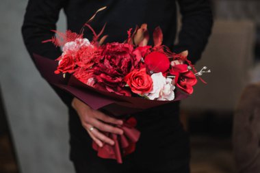 Genç bir adam siyah kazak ve beyaz gömlek bir buket kırmızı çiçek tutuyor.